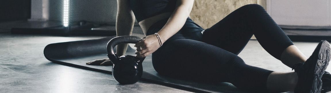 Stylized Photo of Woman Sitting on Yoga Matt Reaching for a Kettlebell