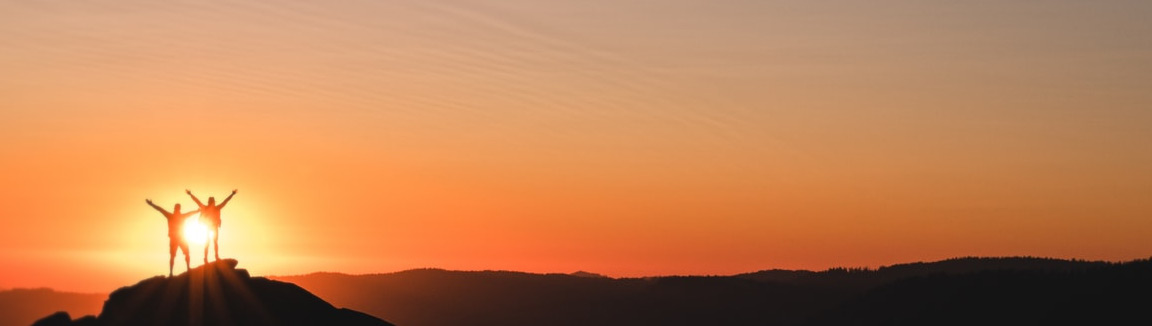 Stylized Photo of Two People Celebrating as Silhouttes in Front of a Sunset